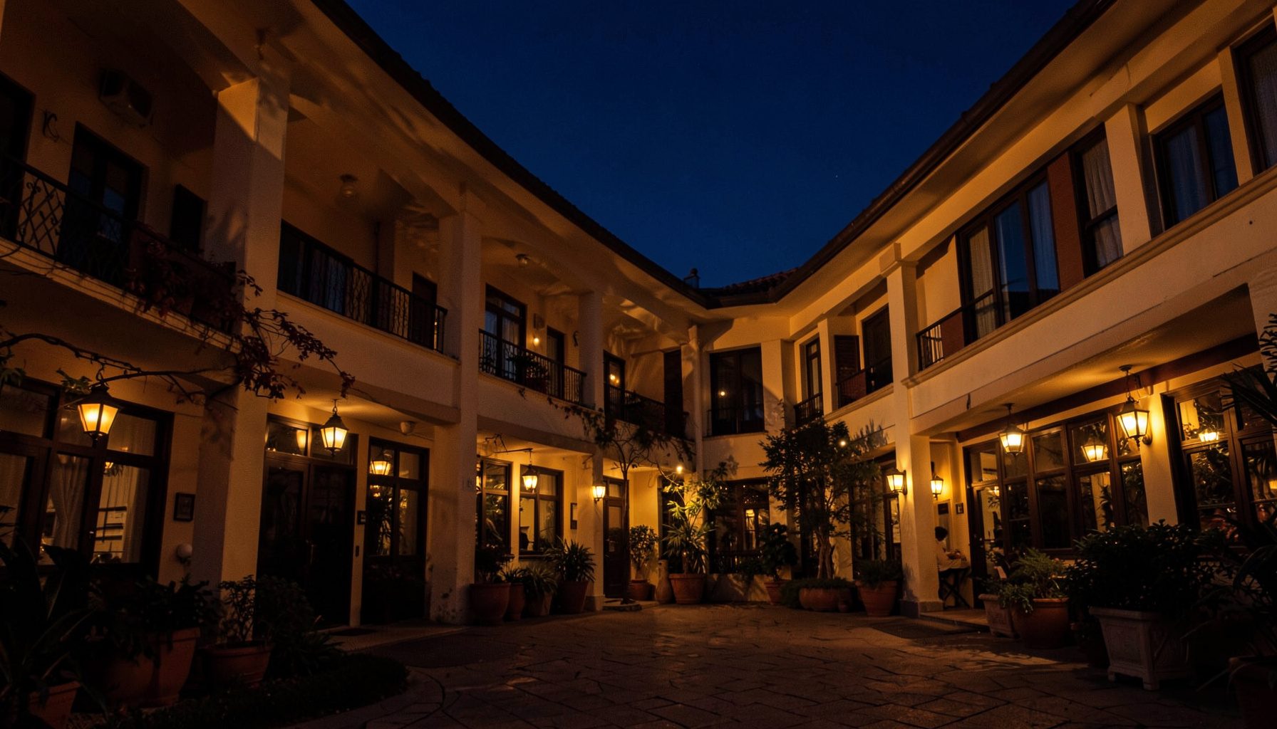 Warm golden-hour photo of a hotel courtyard with warm lantern-like lighting and navy evening sky
