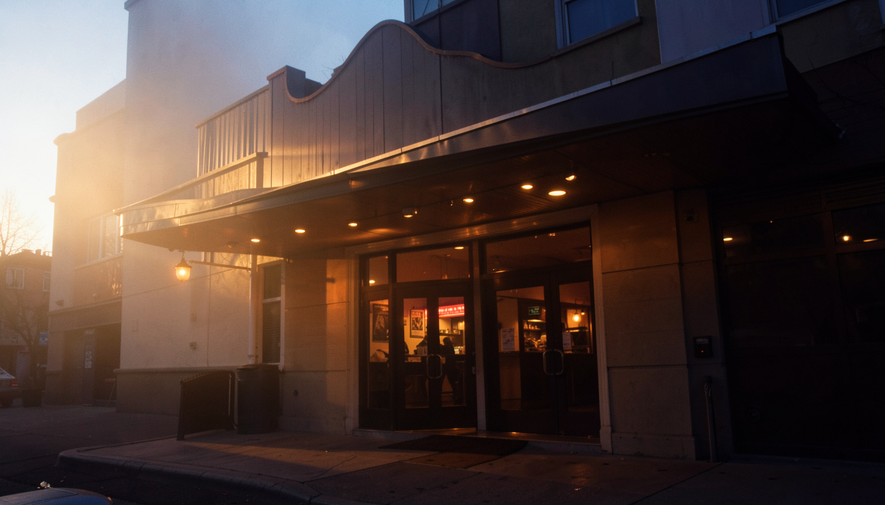Warm golden-hour photo of a cinema hall entrance with warm glowing lights at dusk